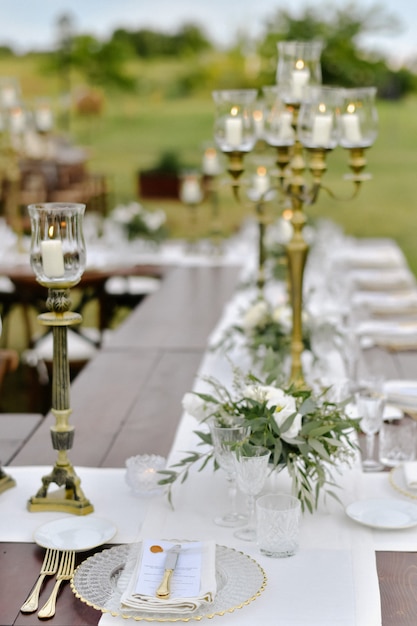 Mesa de celebración de bodas decorada con asientos para invitados al aire libre en los jardines con velas encendidas