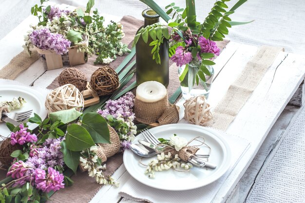 Mesa decorada maravillosamente elegante para vacaciones con flores de primavera y verdes - boda o día de San Valentín con cubiertos modernos, arco, vidrio, velas y regalos, horizontal, primer plano, tonificado