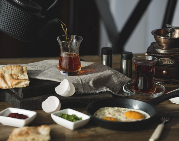Mesa de desayuno para dos personas con vasos de té y huevos fritos.