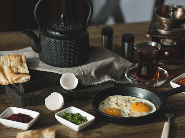 Mesa de desayuno con huevos fritos, hierbas y un vaso de té.