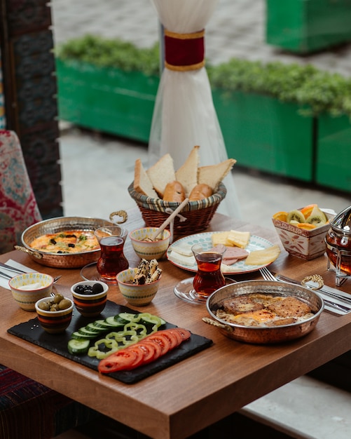 Mesa de desayuno con variedad de alimentos, queso, verduras, tortillas, salchichas, miel y aceitunas.