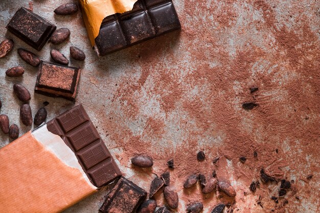 Mesa desordenada con granos de cacao y barra de chocolate y piezas en mesa rústica