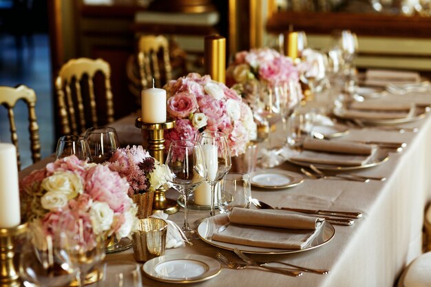 Mesa larga servida con vajilla de porcelana y cubiertos brillantes servidos con flores rosas