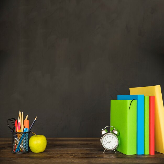 Mesa con libros de texto reloj despertador papelería y manzana