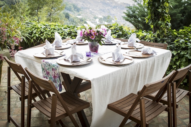 Mesa llena de platos y un florero en un hermoso balcón con una vista increíble.