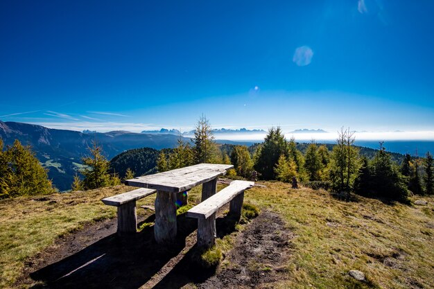 Mesa de madera con bancos rodeados por los Alpes italianos cubiertos de vegetación bajo la luz del sol