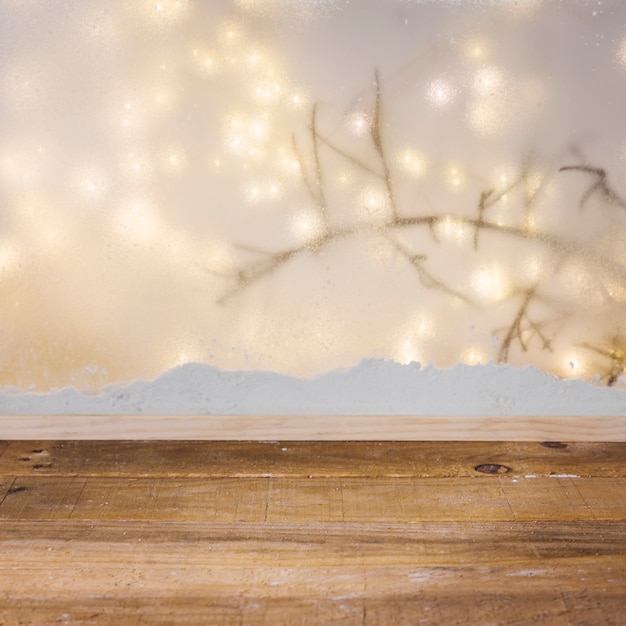 Mesa de madera cerca de banco de nieve, rama de planta y luces de hadas