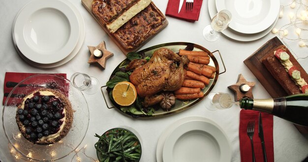 Mesa navideña con pollo asado, pan de patata, pastel de crema pastelera de arándanos, pan casero y verduras al vapor listas para la fiesta