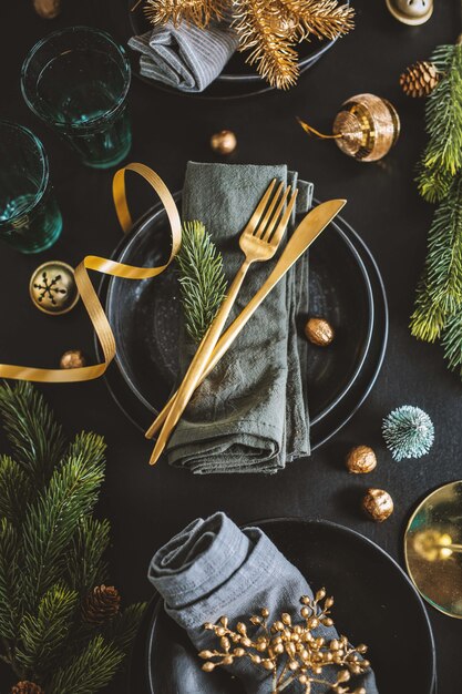 Mesa navideña servida en tonos oscuros con decoración dorada.