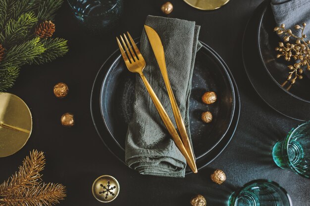 Mesa navideña servida en tonos oscuros con decoración dorada.