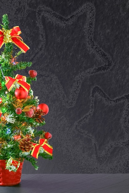 Mesa pequeña árbol de Navidad decorado con adornos rojos y lazos sobre un fondo gris