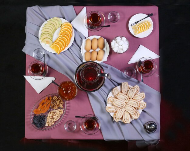 Mesa de té con té y una variedad de dulces y aperitivos sobre el mantel violeta.