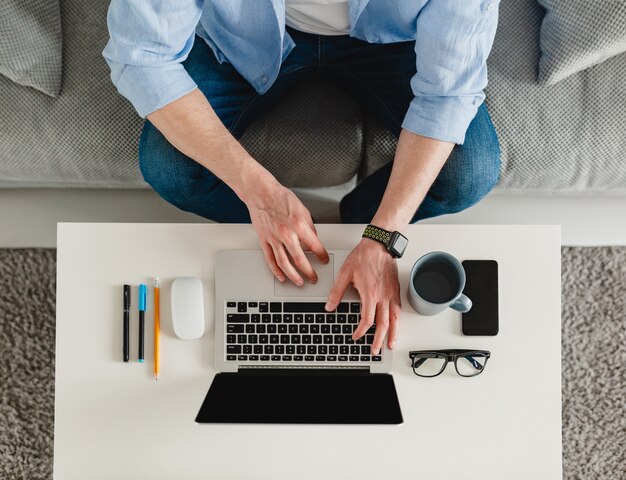 Mesa de trabajo cerca de las manos del hombre en casa trabajando escribiendo en el portátil