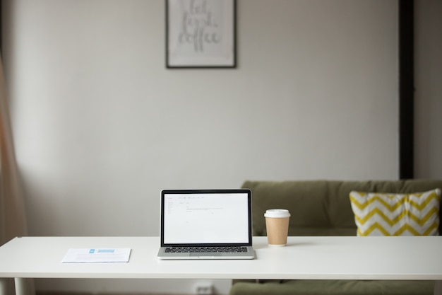 Mesa de trabajo con laptop, café y documentos en interior de casa.