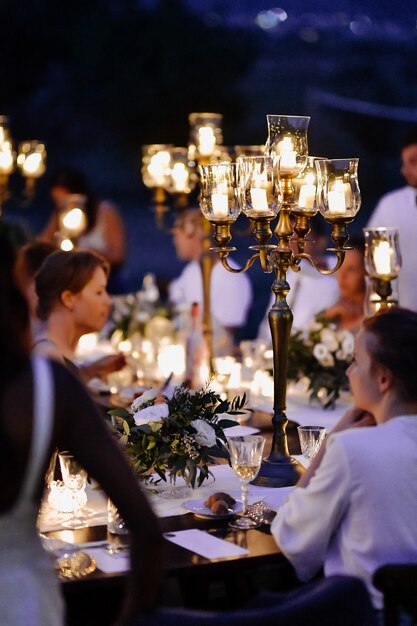 Mesas decoradas con composición floral y candelabros antiguos e invitados en la noche de celebración