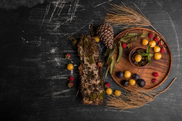 Mezcla de bayas en una bandeja de madera con ramas de roble y conos a un lado en el medio