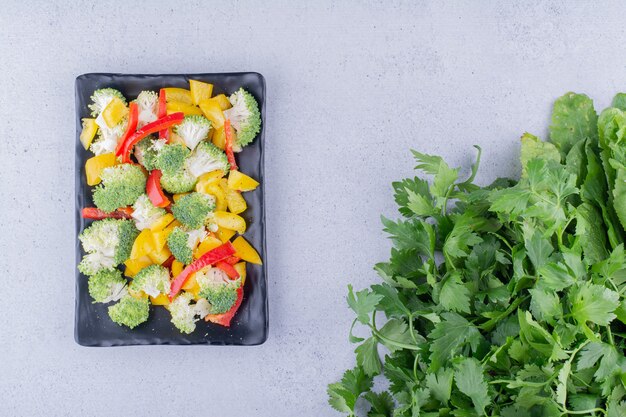 Mezcla de ensalada dietética en un plato negro junto al paquete de perejil sobre fondo de mármol. Foto de alta calidad