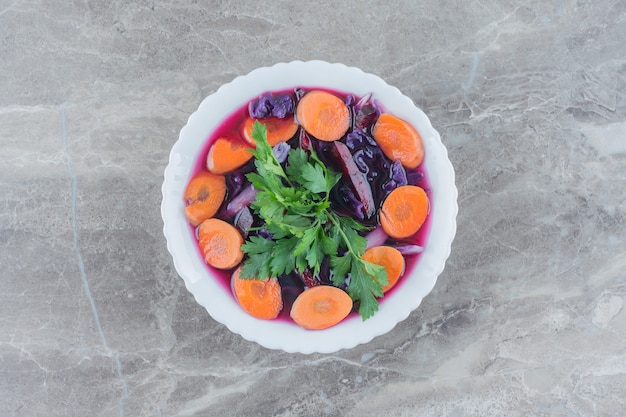 Mezcla de ensalada dietética de remolacha, rodajas de zanahoria y guarnición de perejil en un recipiente sobre mármol.