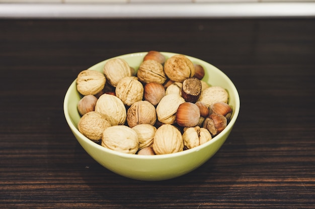 Mezcla de nueces y avellanas en un recipiente amarillo sobre una mesa de madera