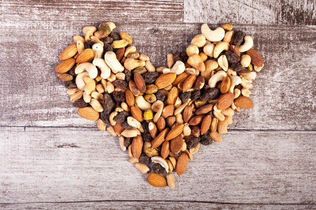 Mezcla de nueces crudas saludables en forma de corazón sobre fondo de madera en foto de estudio. Merienda orgánica saludable