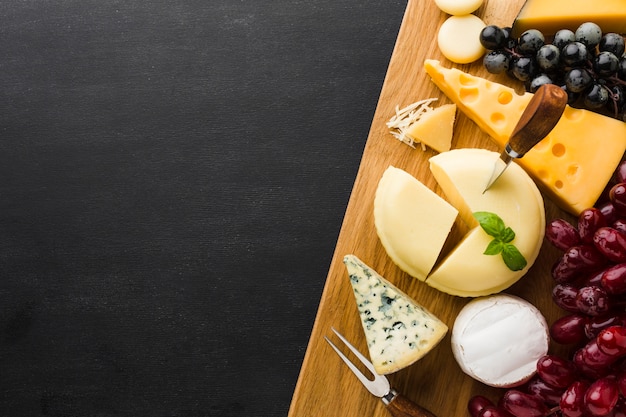 Mezcla plana de queso gourmet y uvas en tabla de cortar con espacio de copia