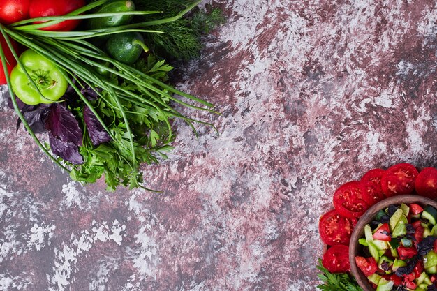 Mezcla de verduras aislada sobre un trozo de mármol con una taza de ensalada a un lado en ambos ángulos.