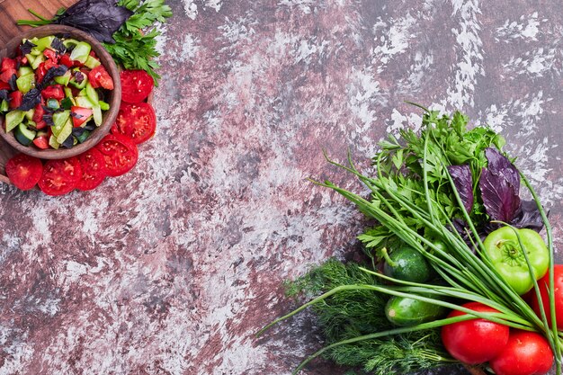 Mezcla de verduras aislado en un trozo de mármol con una taza de ensalada a un lado