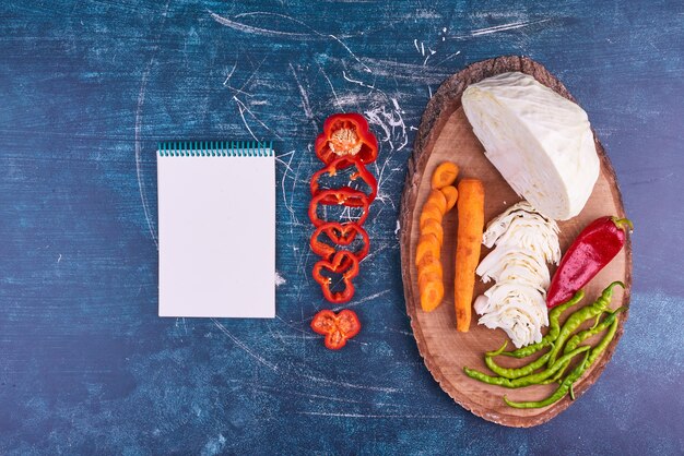 Mezcla de verduras en un plato de madera con un cuaderno a un lado.