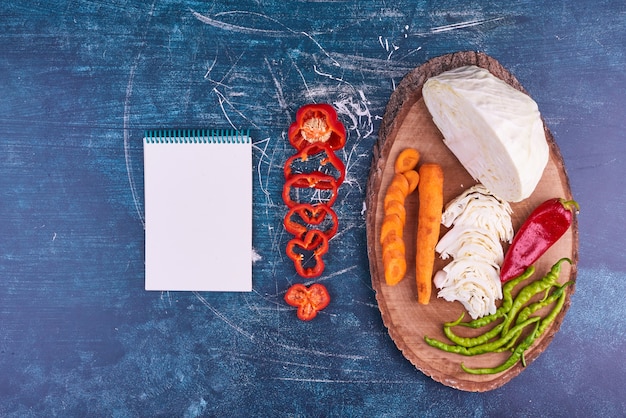 Mezcla de verduras en un plato de madera con un cuaderno a un lado.