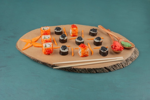 Mezcle sushi y cucharadas de jengibre encurtido y wasabi sobre una tabla de madera.