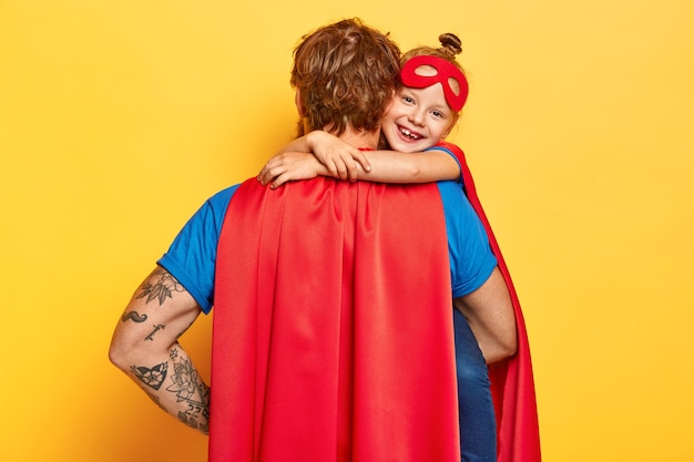 Mi adorable super papá. Niño pequeño cariñoso abraza a padre con amor, usa máscara roja