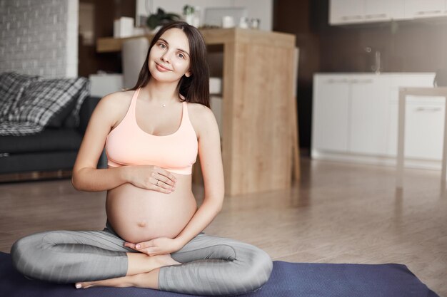 Mi bebé practicando yoga conmigo Captura interior de una mujer embarazada feliz y orgullosa esperando que nazca un bebé sentada en una almohadilla rodante con ropa deportiva haciendo ejercicio tocando el vientre con ternura