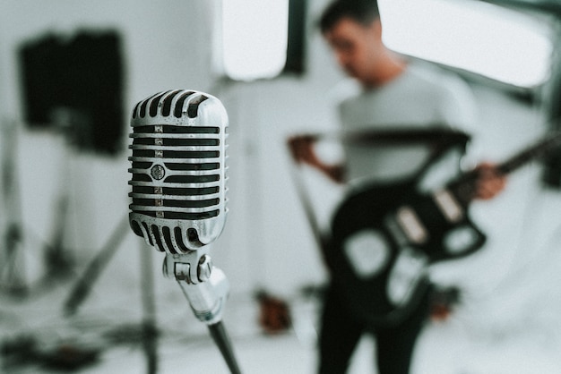 Micrófono de condensador de diafragma grande con un músico sosteniendo una guitarra eléctrica en el fondo