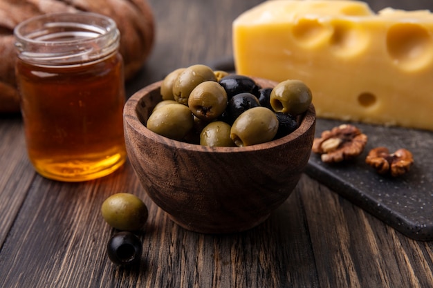 Miel de vista frontal en un tarro con queso maasdam en un soporte y aceitunas en la mesa