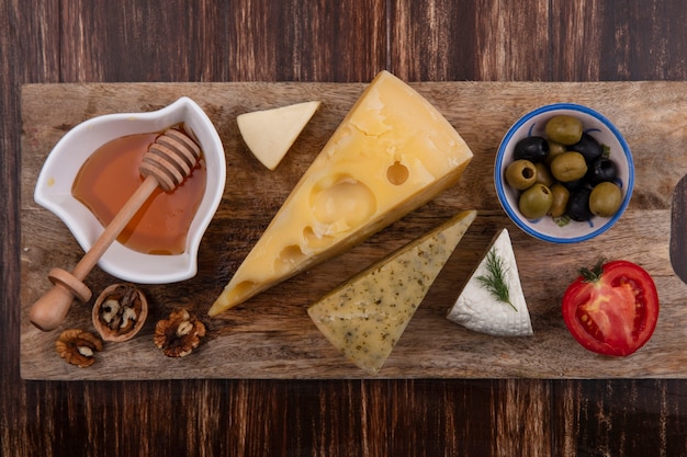 Miel de vista superior con variedades de quesos, aceitunas y tomate en un soporte sobre un fondo de madera