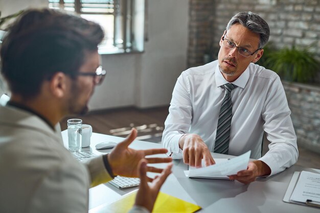 Miembro del equipo de recursos humanos hablando con un candidato mientras revisa su currículum durante una entrevista de trabajo en la oficina