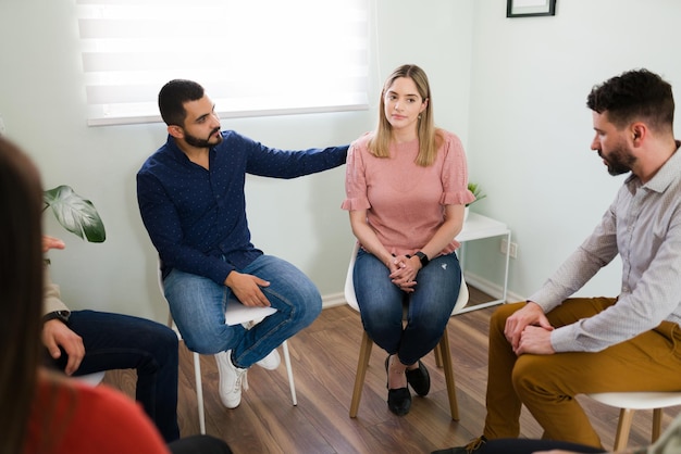 Miembro masculino en una reunión de AA consolando a una mujer caucásica durante una sesión de terapia de grupo. Mujer bonita triste que asiste a un grupo de apoyo