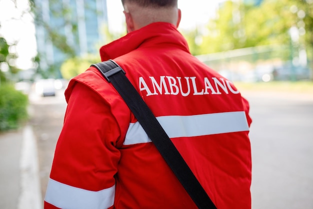 Miembro del personal de ambulancia desde atrás con su mochila de emergencia y monitor de signos vitales Ambulancia escrita en su espalda