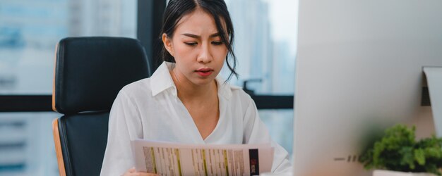 Milenaria joven empresaria china trabajando estresarse con el problema de investigación del proyecto en el escritorio de la computadora en la sala de reuniones en la pequeña oficina moderna Concepto de síndrome de burnout ocupacional de personas de Asia.