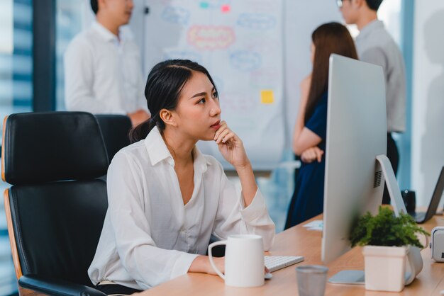 Milenaria joven empresaria china trabajando estresarse con el problema de investigación del proyecto en el escritorio de la computadora en la sala de reuniones en la pequeña oficina moderna Concepto de síndrome de burnout ocupacional de personas de Asia.