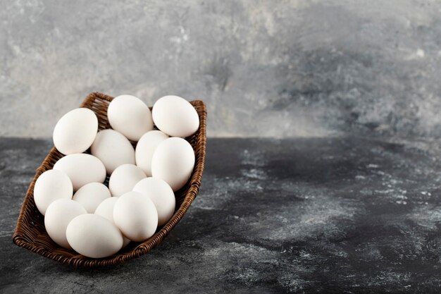 Un mimbre de madera lleno de huevos de gallina cruda blanca.