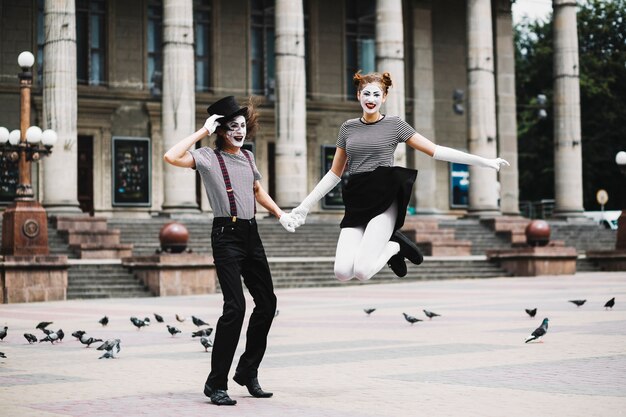 Mime femenino sonriente que sostiene la mano del mime masculino que salta delante del edificio