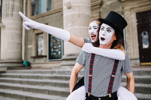 Mime masculino dando paseo en tándem a mime femenino apuntando a algo