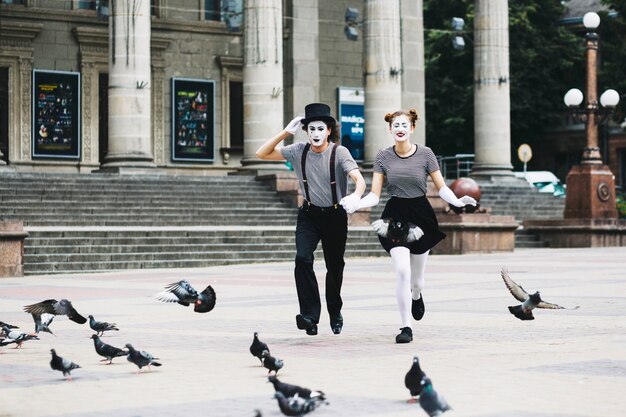 Mime pareja cogidos de la mano corriendo frente al edificio