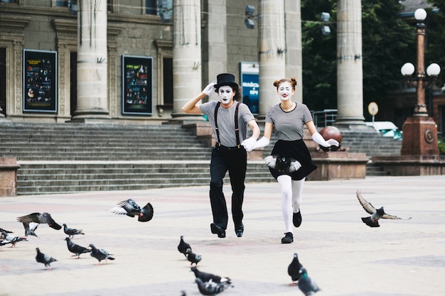 Mime pareja cogidos de la mano corriendo frente al edificio