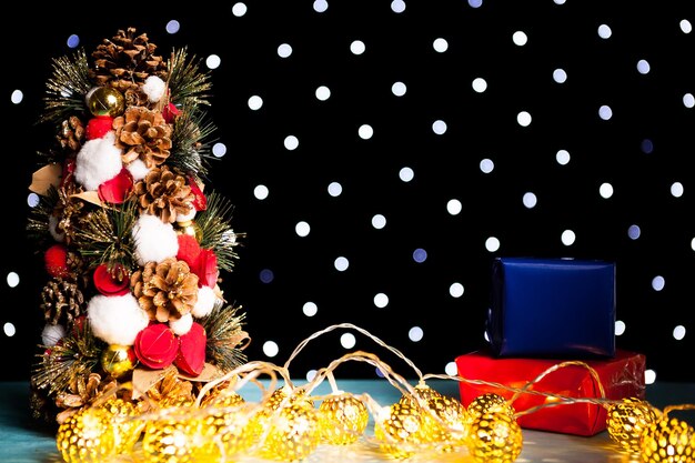 Mini árbol de Navidad y dos regalos de caja de colores en la luz festiva del bokeh. Decoración y vacaciones. Temporada y año nuevo