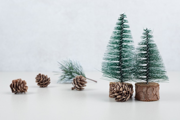 Mini árboles de Navidad y piñas en superficie beige.