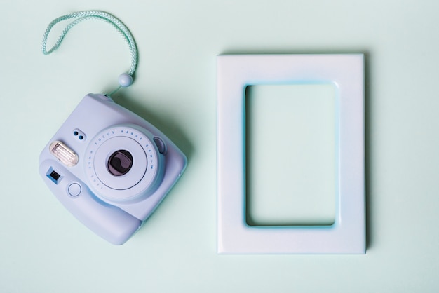 Foto gratuita mini cámara instantánea y marco de borde vacío sobre fondo azul