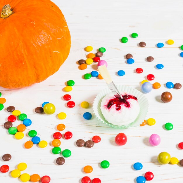 Mini muffin entre pequeños caramelos cerca de calabaza