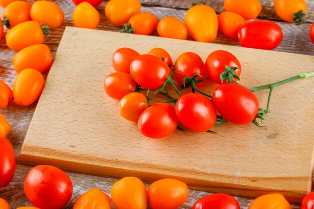 Mini tomates alto ángulo de vista sobre tabla de cortar y madera